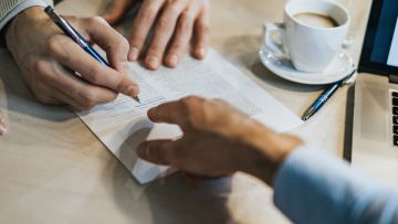 Primer plano de unas manos de dos hombres señalando un documento en papel