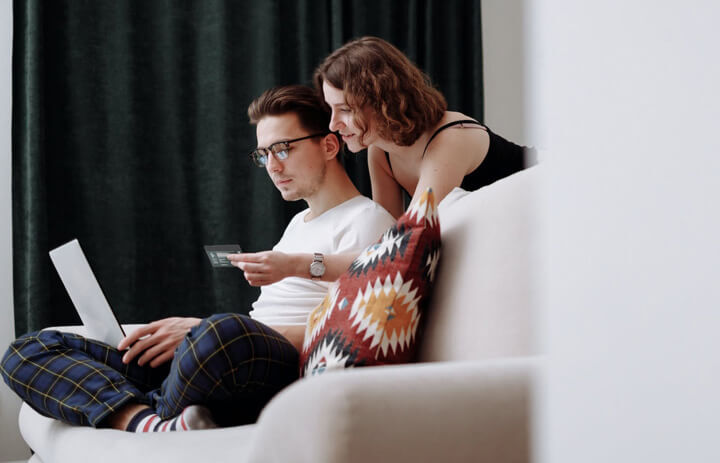 Chico y chica sentados en un sofa apunto de pagar con tarjeta