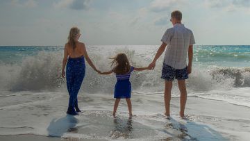 Familia de tres de espaldas al mar viendo las olas