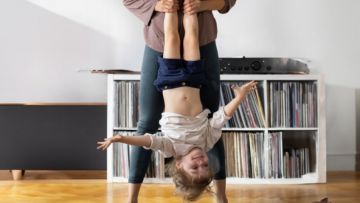 Imagen de un salón de estar en el que una madre está jugando con su hija, sonriente, sujetándola por los pies.