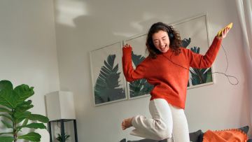 Chica saltando de alegría escuchando música desde su teléfono móvil.