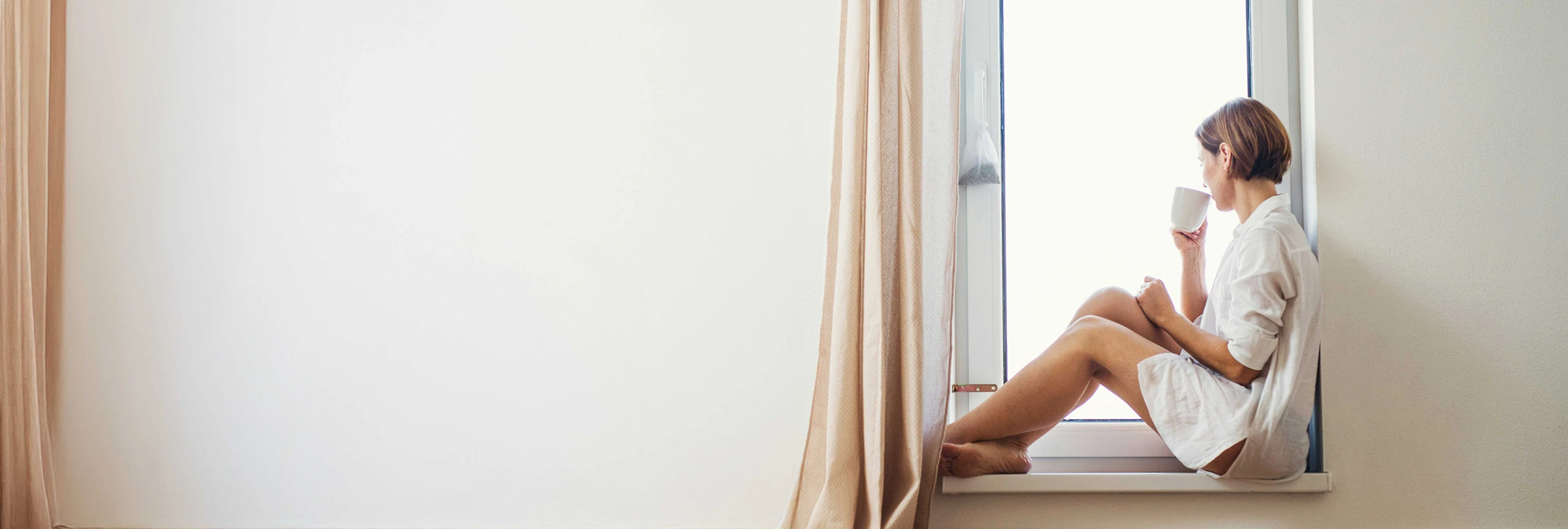Mujer sentada junto a la ventana tomando un café