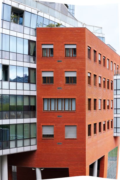 Edificio de viviendas que combina fachada de ladrillo rojo y cristal, con persianas en algunas ventanas.